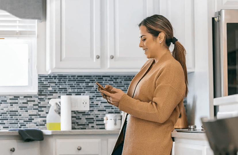 Woman smiling while checking her Momentum debt settlement progress on her phone in her kitchen